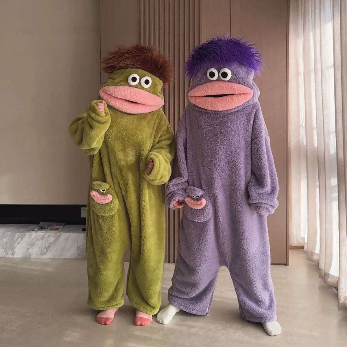 Two people wearing sage green and purple Big Mouth Monster onesies together